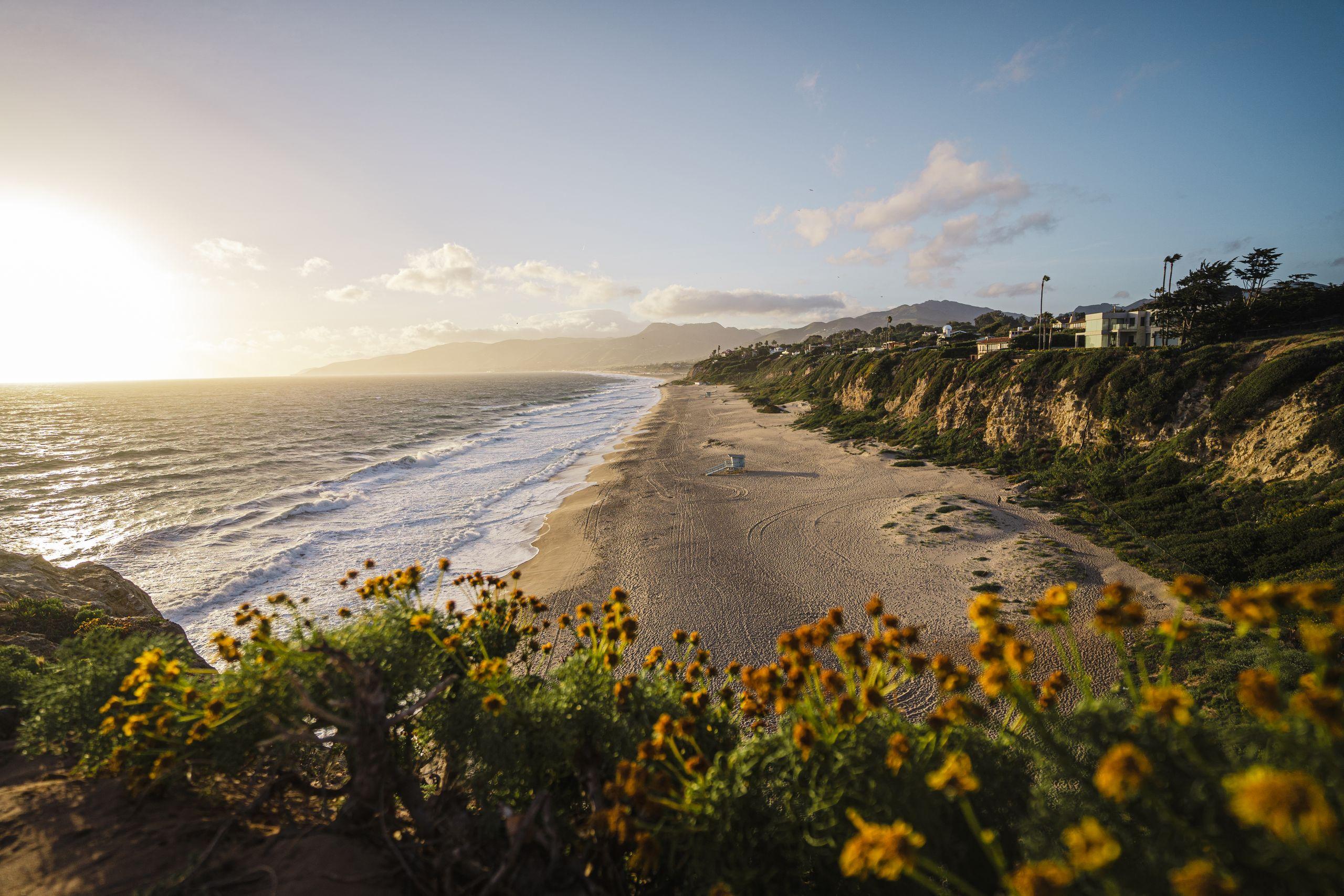 The Malibu coastline at golden hour: an empty beach below cliffs lined with oceanfront homes