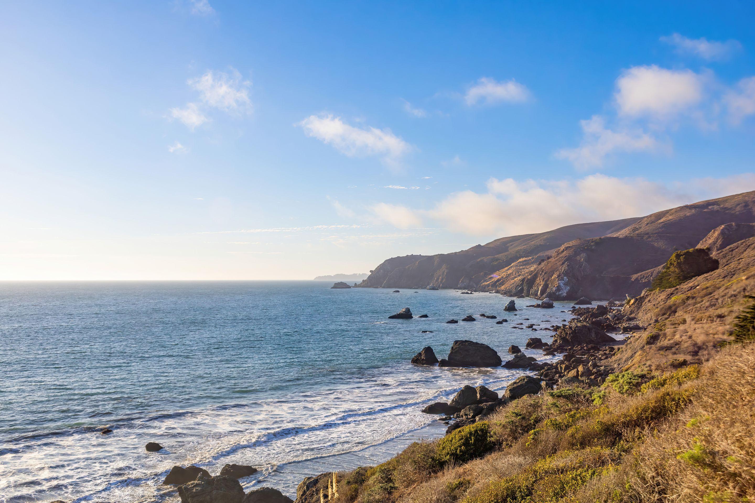 A green headland dropping to a wide blue bay under a clear sky