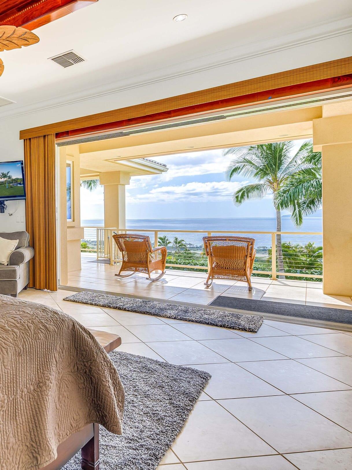 A bedroom opening onto a lanai with two chairs facing the ocean at Maui Recovery in Lahaina