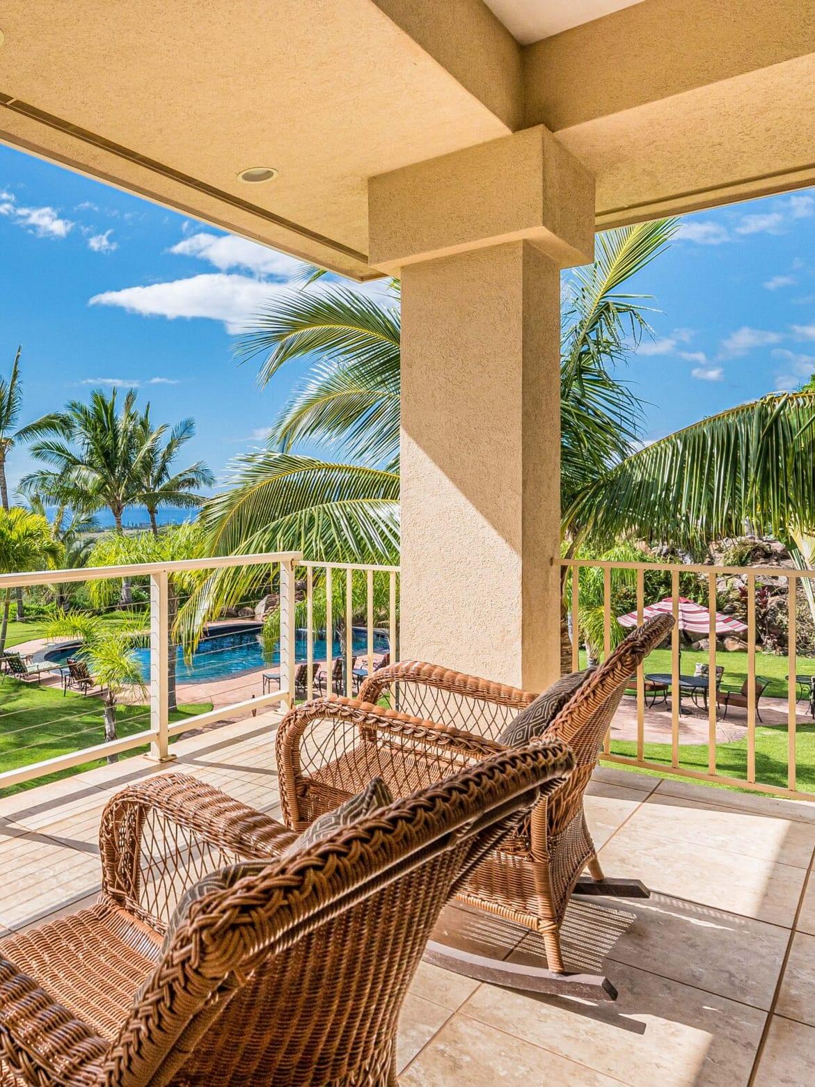Wicker chairs on a covered lanai above a pool, palms and the ocean at Maui Recovery in Lahaina