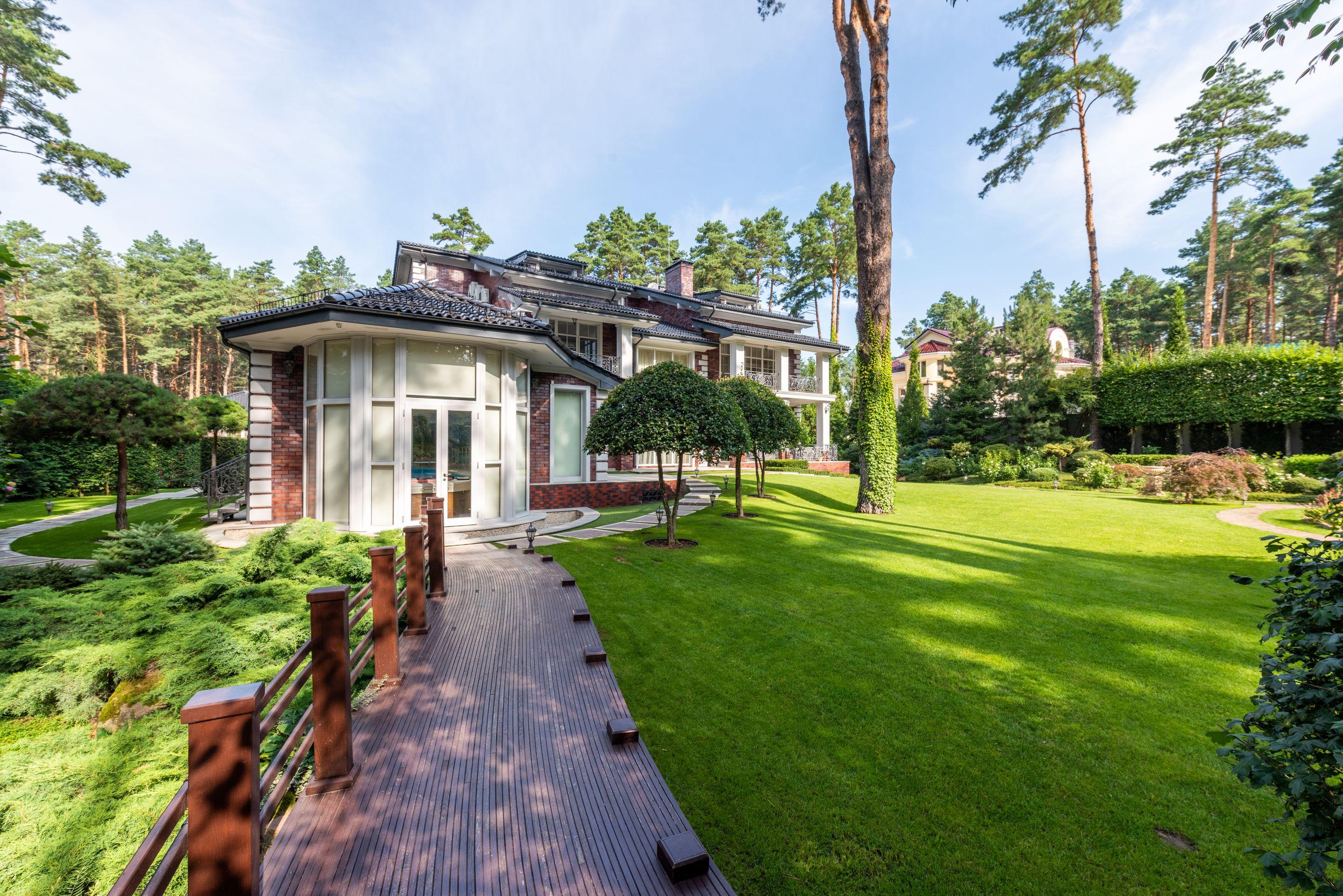 A low house set back across a wide green lawn edged with tall pines under a blue sky