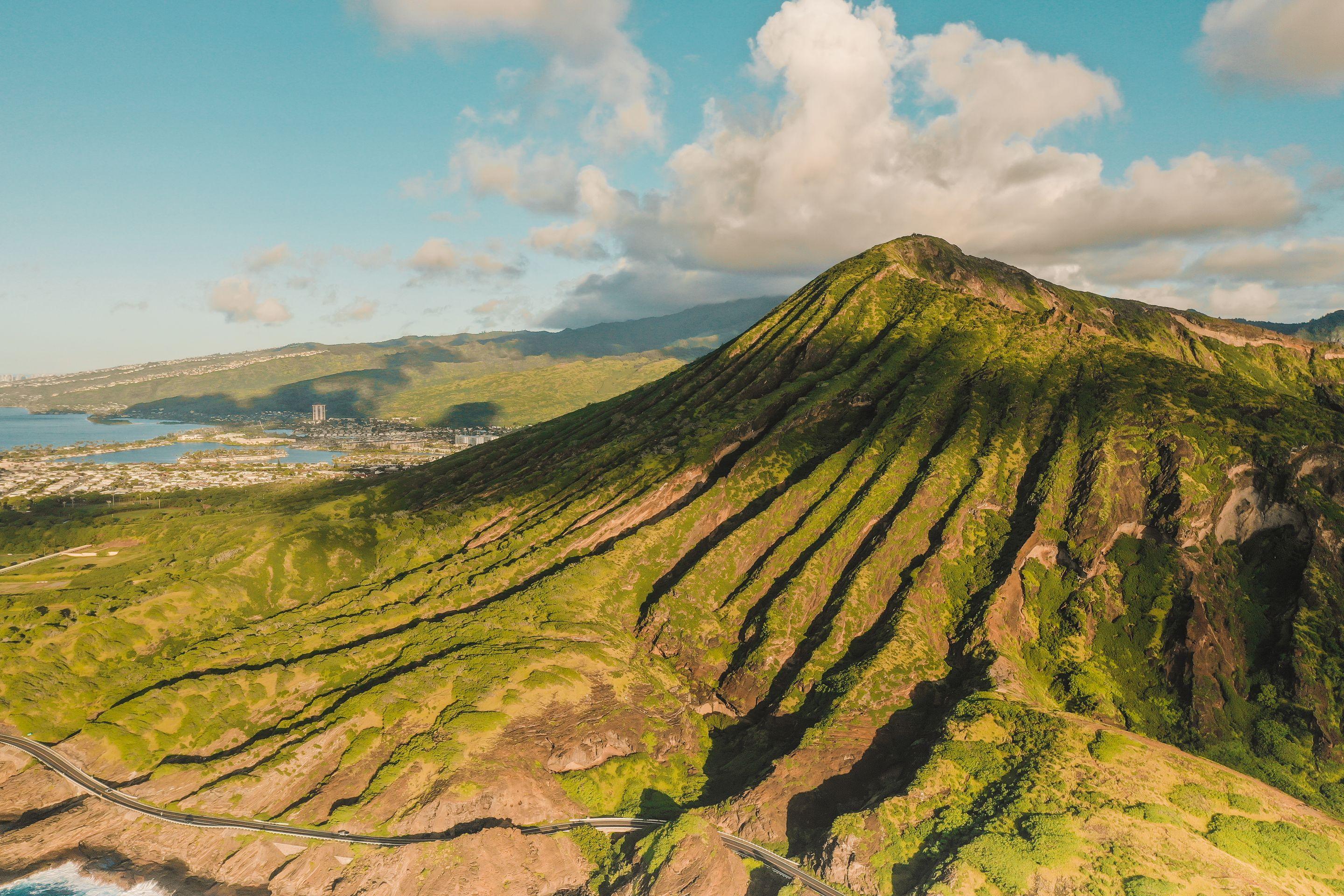 A green volcanic crater rising above the coast under a blue sky with white cloud