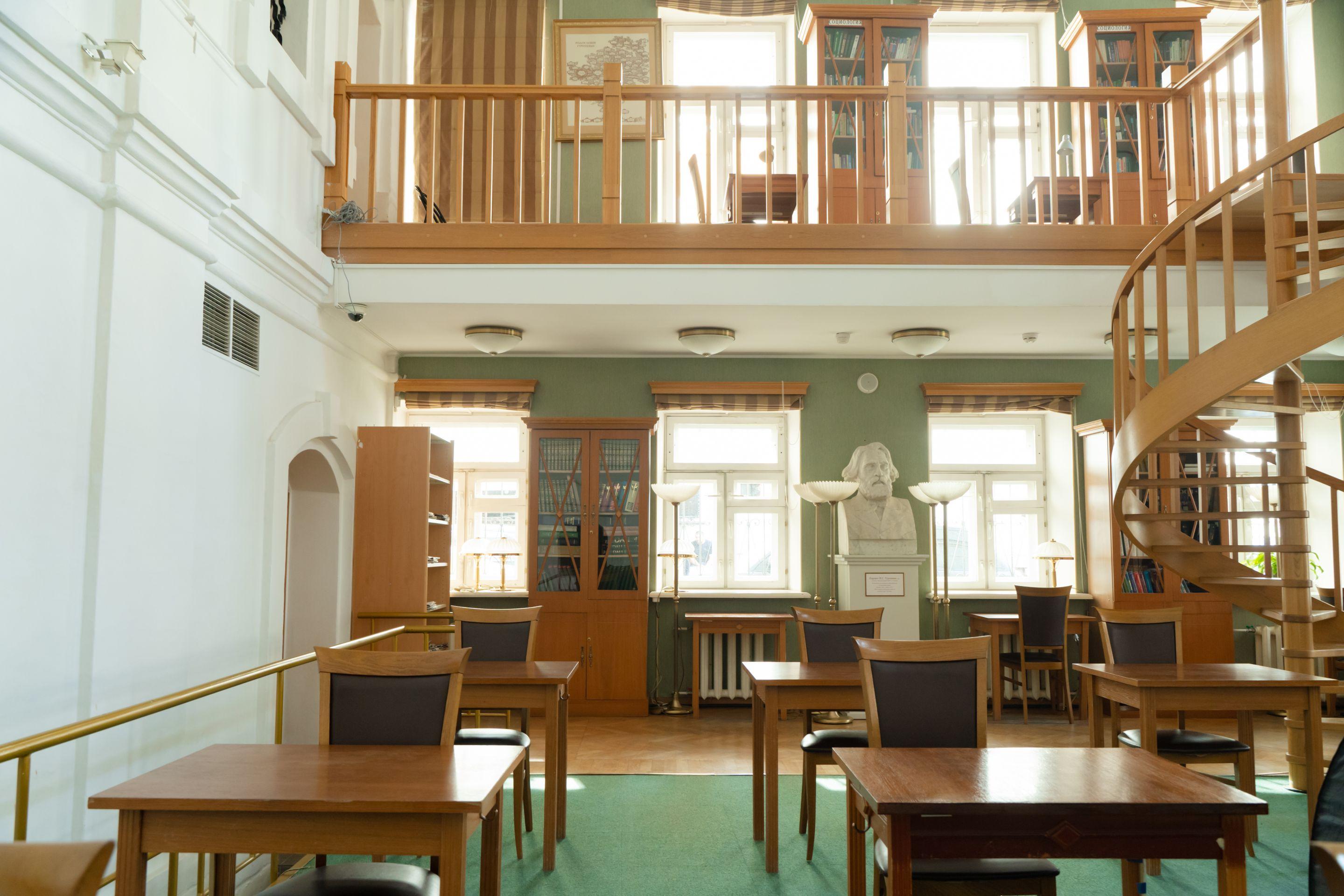 A bright reading room with wooden tables, tall windows and a spiral staircase, no one in it