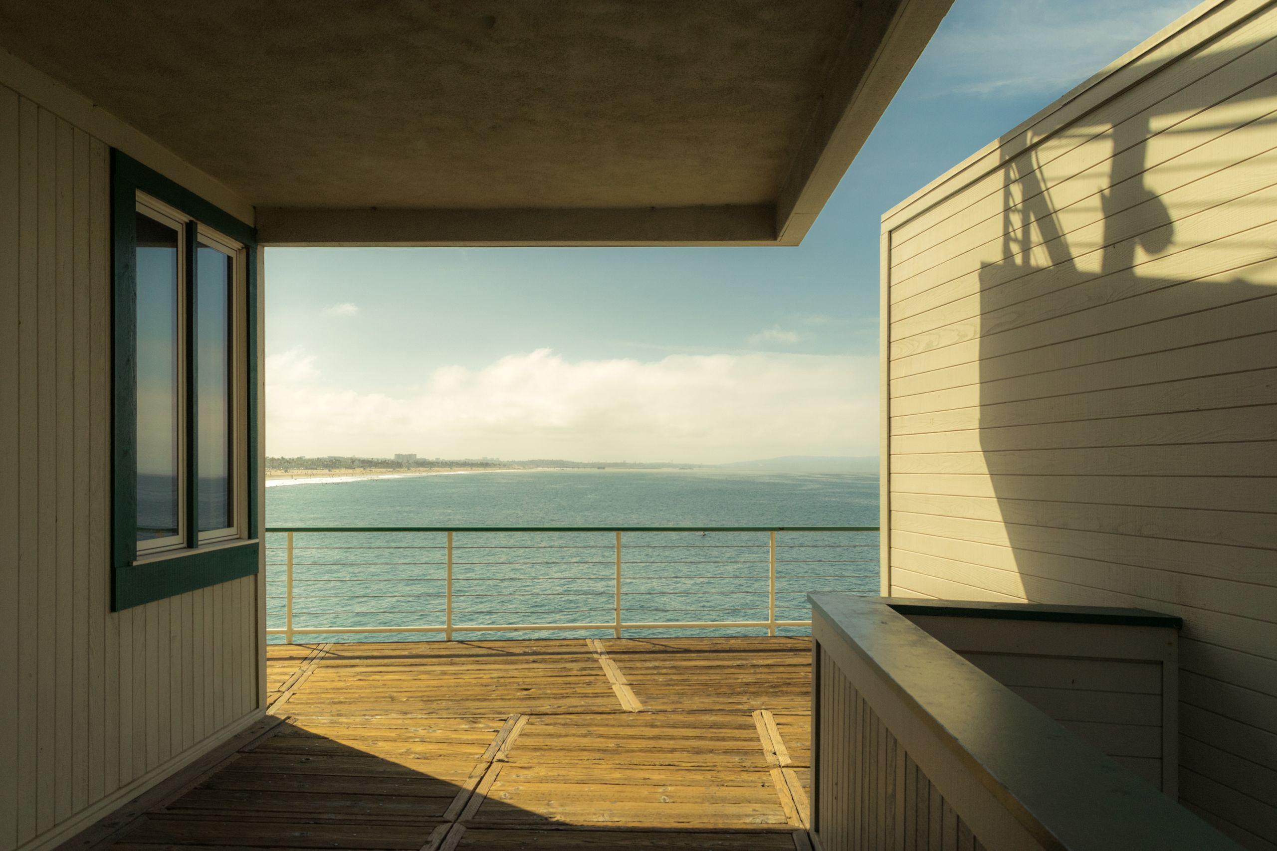 A wooden deck terrace overlooking calm ocean water in bright sunlight
