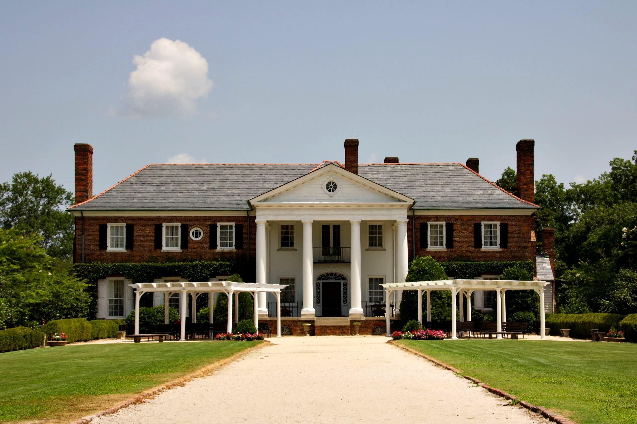 A grand colonnaded estate with white columns and manicured grounds under a bright blue sky