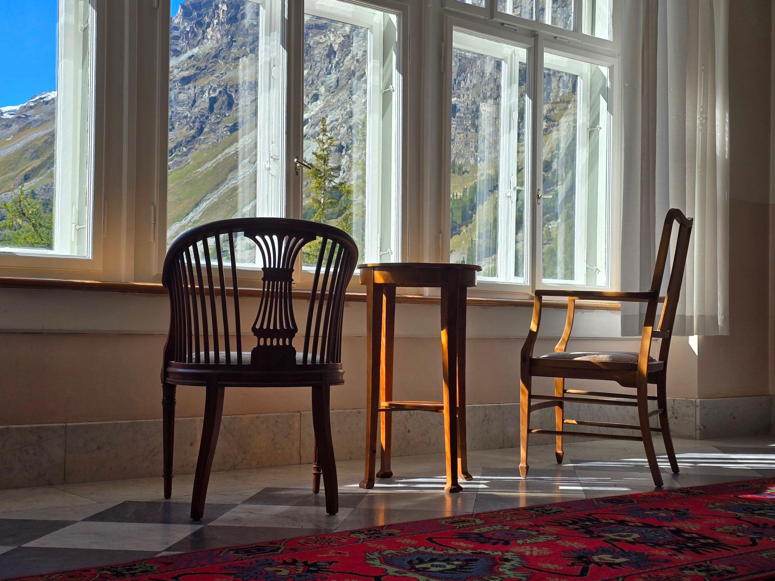 Two antique chairs at a tall window overlooking an alpine landscape, the register of considered residential space