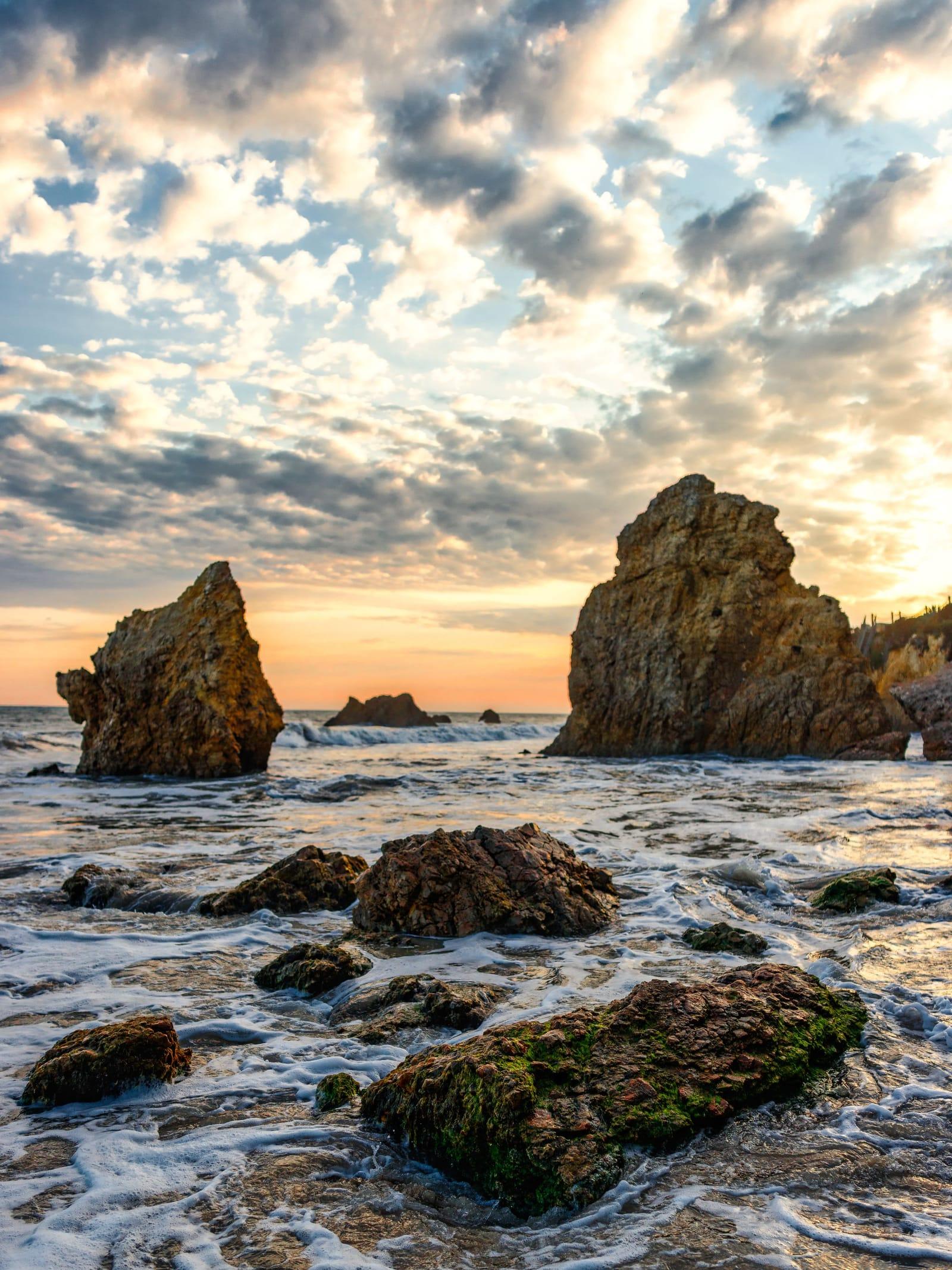Rocks and tide pools off the Malibu coast under a sunset sky of scattered cloud